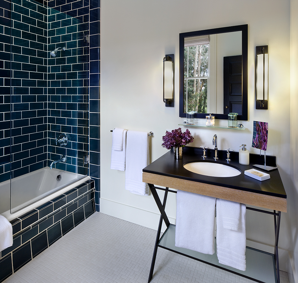The Presidio Trust Inn at the Presidio, San Francisco, CA: Hospitality and Historic renovation by Herrero Builders preserving a National Historic Landmark, with Architectural Resources Group. Interior view of a bathroom with a dark blue tiled tub surround and a console sink.