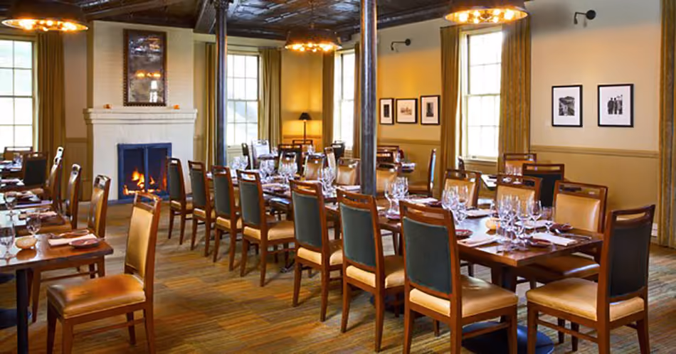 Fort Baker Retreat Group Murray Circle Restaurant, Sausalito, CA: Hospitality and Historic renovation and new construction by Herrero Builders, with Leddy Maytum Stacy Architects. Interior view of a long communal table set beside a lit fireplace.