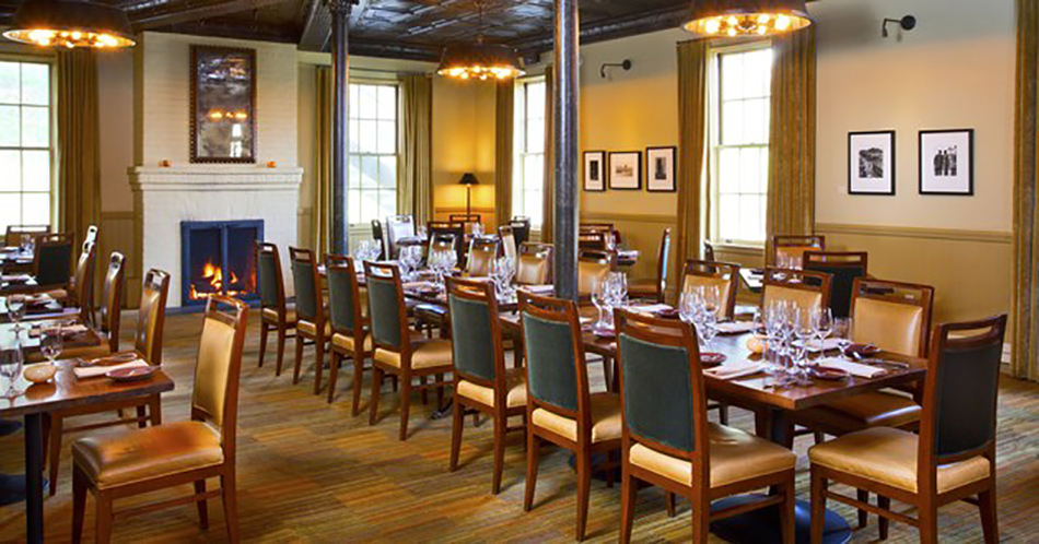 Fort Baker Retreat Group Murray Circle Restaurant, Sausalito, CA: Hospitality and Historic renovation and new construction by Herrero Builders, with Leddy Maytum Stacy Architects. Interior view of a long communal table set beside a lit fireplace.
