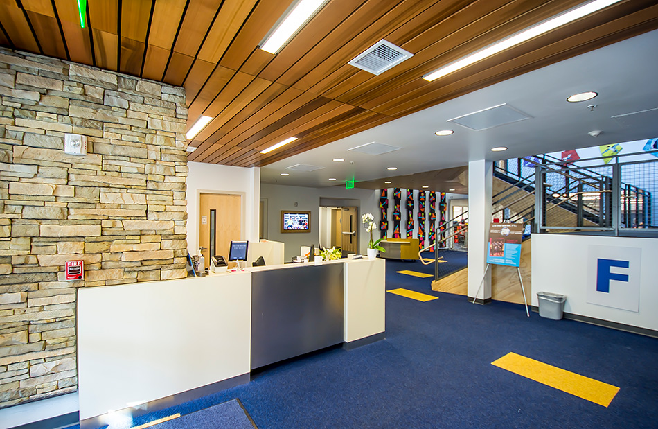 Town School for Boys Core Building & West Wing Excavation, San Francisco, CA: Education New Construction by Herrero Builders with significant excavation on an occupied campus, with MKThink. Interior view of the foyer reception desk with a stone feature wall and wood slat ceiling.