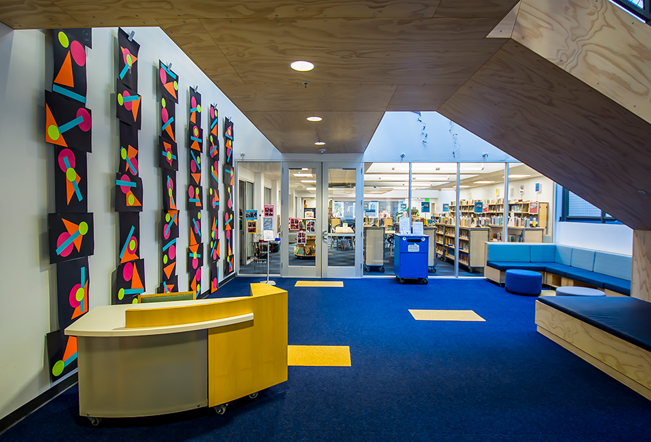 Town School for Boys Core Building & West Wing Excavation, San Francisco, CA: Education New Construction by Herrero Builders with significant excavation on an occupied campus, with MKThink. Interior view of a lobby with a wood reception desk, geometric wall artwork and a plywood stair soffit.