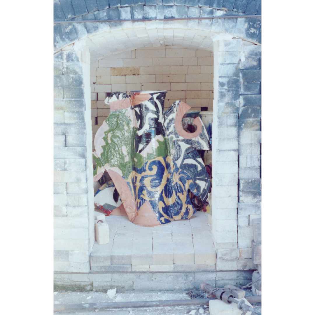 L to R: 1: Still Life Vase in kiln, Boulder, Colorado, 1991 | 2: Betty and kiln, Boulder, Colorado, March 1970 | 3: Betty and kiln, Boulder, Colorado, May 1965 | 4: “Folded Tri-part Vase,” 1975, 8 x 25 x 8 in. Salt glazed stoneware | 5: Betty and kiln, Boulder, Colorado, c. 1960s | 6: Kiln, Antella, Italy, c. 1990s | 7: Kiln, Antella, Italy, c. 1996 | 8: Kiln, Antella, Italy, c. 1990s | 9: Betty and kiln, Antella, Italy, c. 1990s | 10: Betty and George firing the kiln, Antella, Italy, c. 1973 | 11: “Pillow Pitcher: Italian,” 1977, 15 x 30 x 15 in. Terra sigillata | 12: Betty and kiln, Antella, Italy, c. 1960s | 13: Betty and kiln, Antella, Italy, c. 1969 | 14: “Fabric Samples” in progress in kiln, New York, New York, 2005 | 15: “Fabric Samples,” 2005, 30 x 31 x 8 in. Glazed earthenware. Installation view from “The Art of Betty Woodman,” Metropolitan Museum of Art, New York, New York, 2006 | 16: Ceramic fragments in the kiln, New York, New York, 2013 | 17: Detail from “Wallpaper 9,” 2015, dimensions variable. Glazed earthenware, epoxy resin, lacquer, acrylic paint | 18: “Vase,” 1955, 5 x 5 x 5 in. Lusterware | 19: Kiln, Albuquerque, New Mexico, 1955. All artworks by Betty Woodman © Woodman Family Foundation / Artists Rights Society (ARS), New York. Woodman Family Foundation Archives.