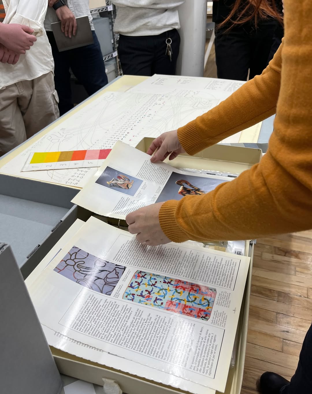 L to R: Micaela shows the Pratt class a magazine article on George Woodman and Betty Woodman. Photo by Cristina Pattuelli. | Detail of a drawing done by Francesca Woodman with a note to Betty Woodman and George Woodman. The drawing includes a sofa Francesca used as a prop in photographs and teacups likely depict Betty Woodman’s ceramics. Flight information in the note may help us establish timelines for all three artists in the future. | Photo boxes owned by George Woodman. While the boxes are not “archival” (acid free), the information written on them by the artist makes them valuable in establishing provenance of final artworks. | The archive interior. Simple industrial rolling racks are utilized to hold archival assets.