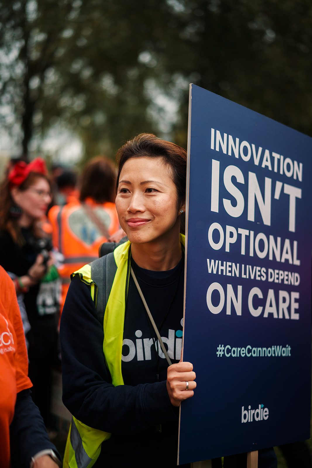 Person wearing yellow vest holding sign saying innovation isn't optional for care with hashtag CareCannotWait.