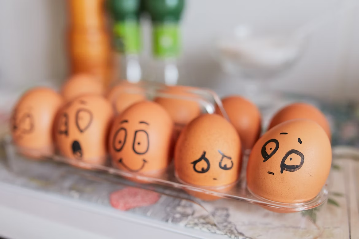 Brown eggs in a clear tray with faces drawn on them showing different emotions.