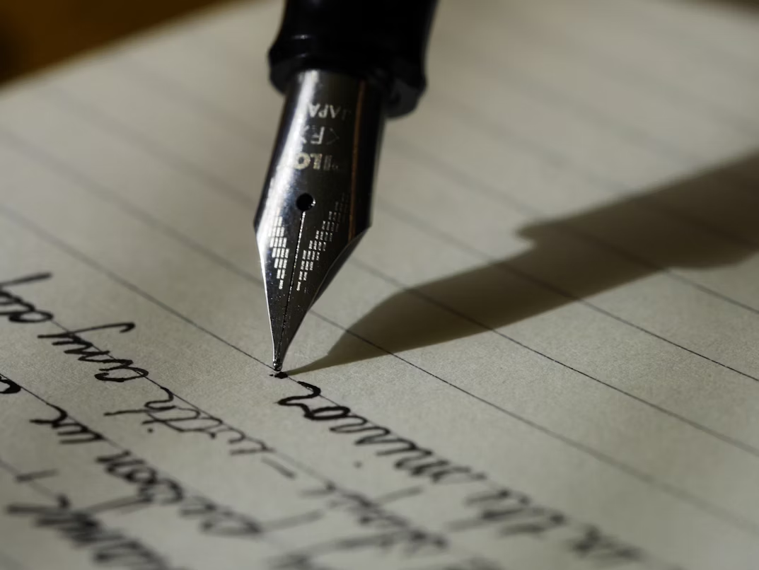 A fountain pen writing on black lined paper.