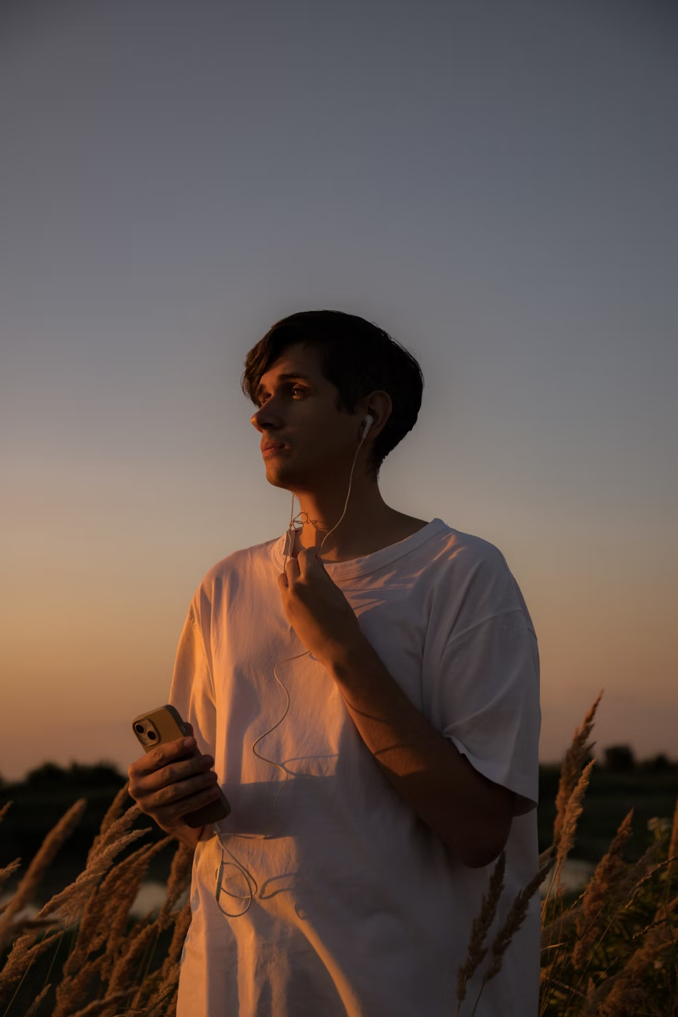 A young man, holding an iPhone, listening to music via wired headphones.
