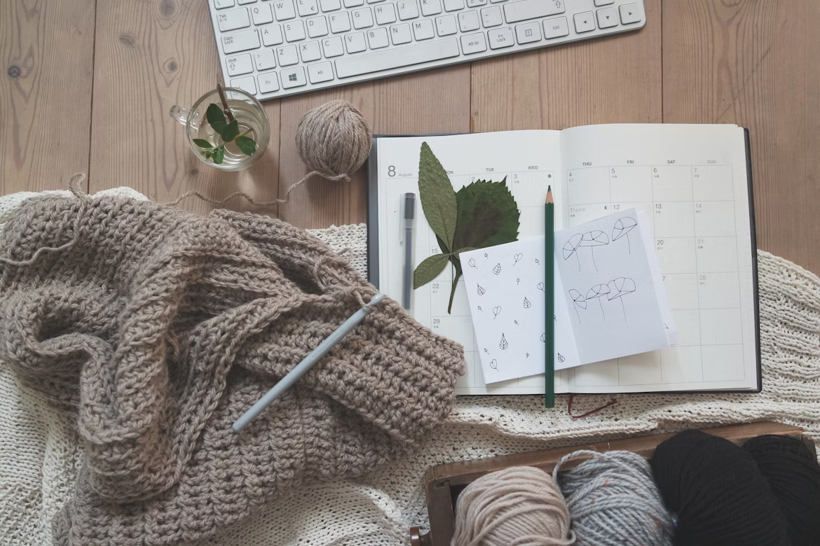 A notebook with a pencil and a woven garment made of yarn on a desk.