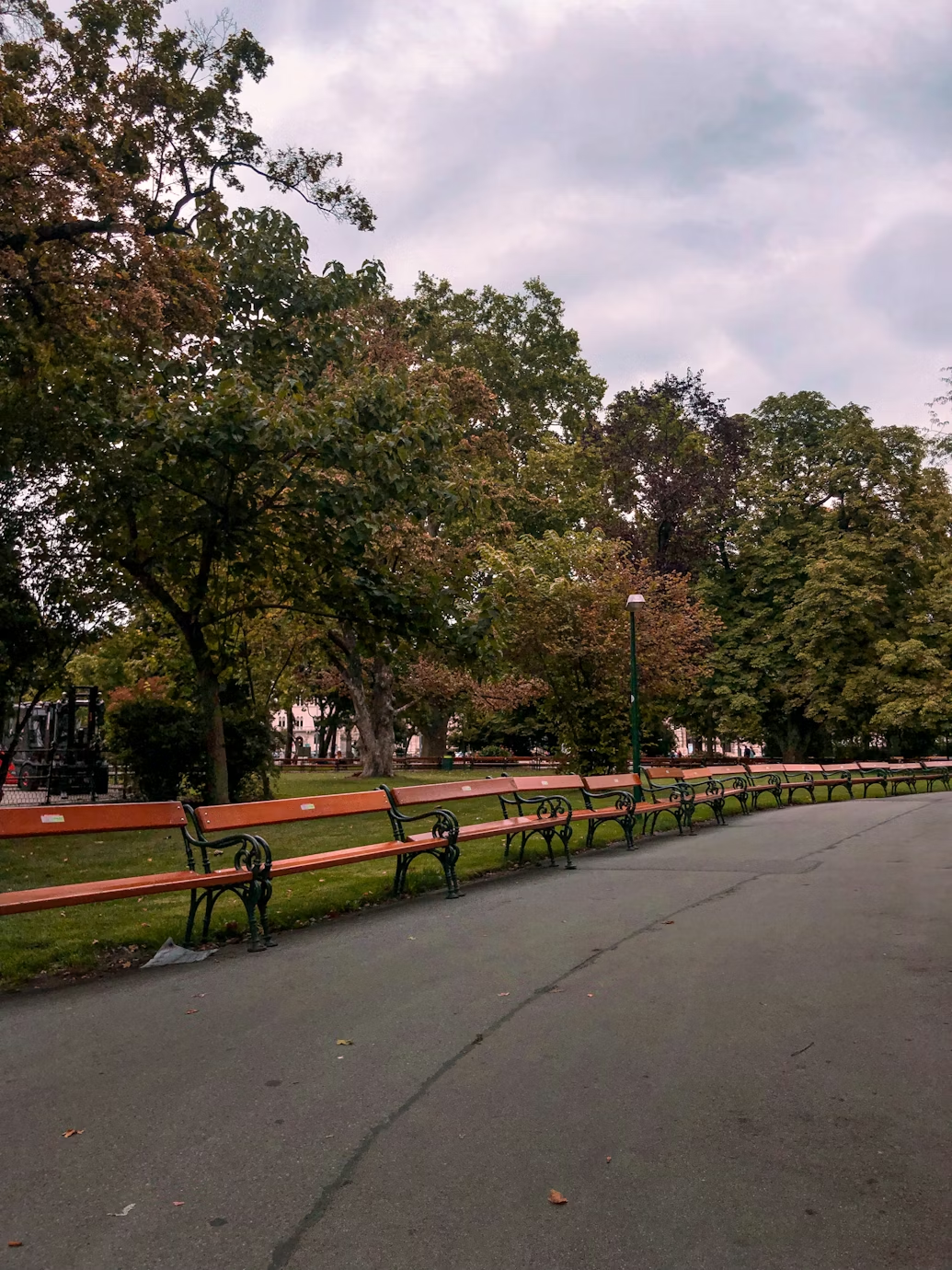 A pathway in a park lined with benches and a lamp post.