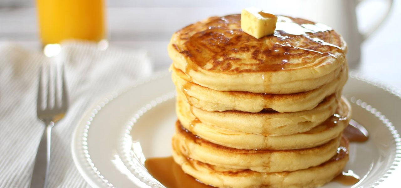 Stack of fluffy pancakes with butter and syrup.