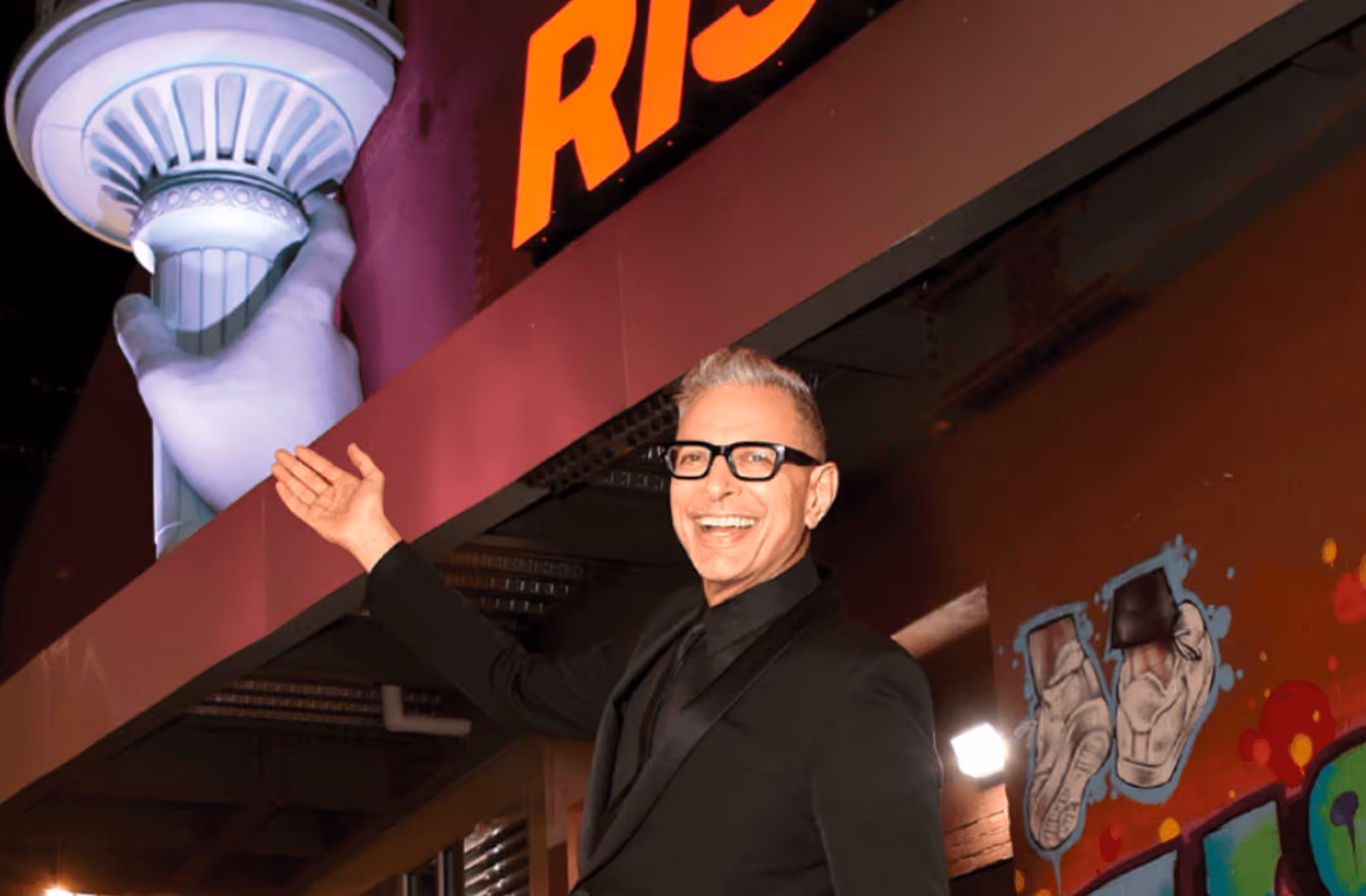 Jeff Goldblum smiling and posing in front of RiseNY