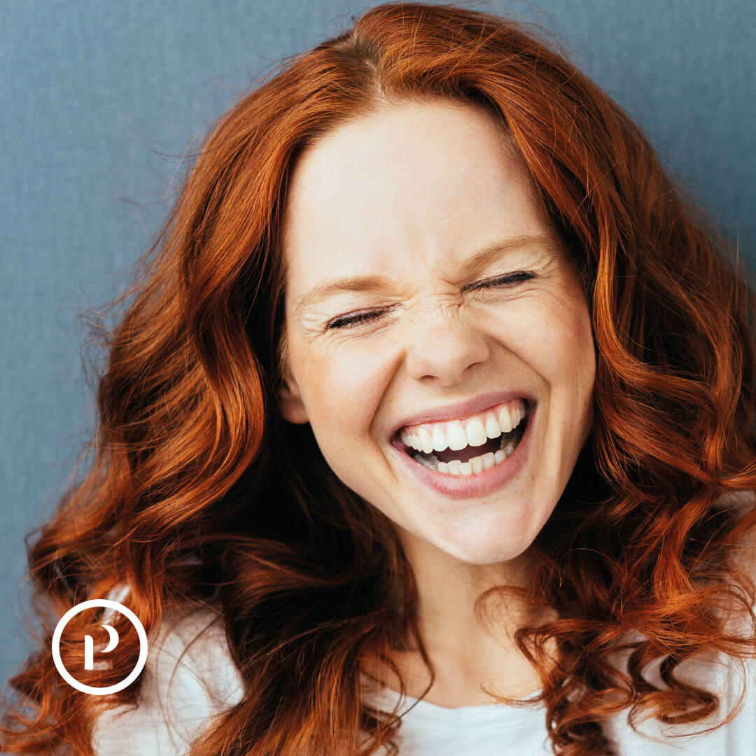 Platineers Smile. Young woman with red hair smiling on grey background.