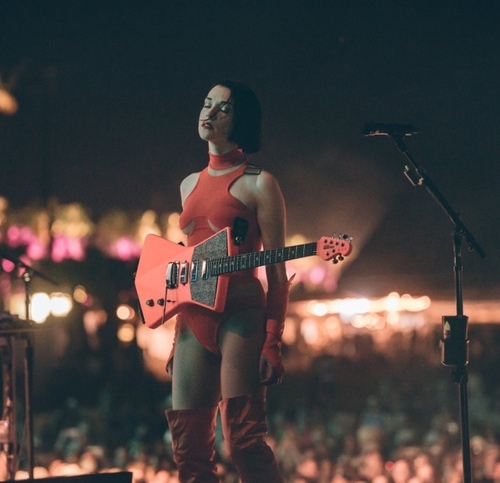 Annie Clarke in an orange leotard holds her signature ernie ball in front of a massive crowd