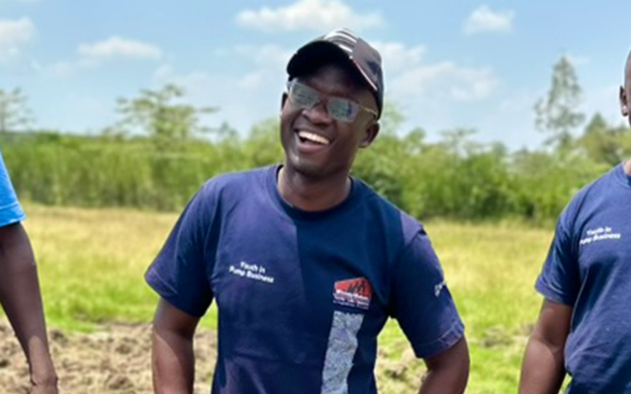 Man stands smiling in a plowed field on a sunny, blue-sky day.