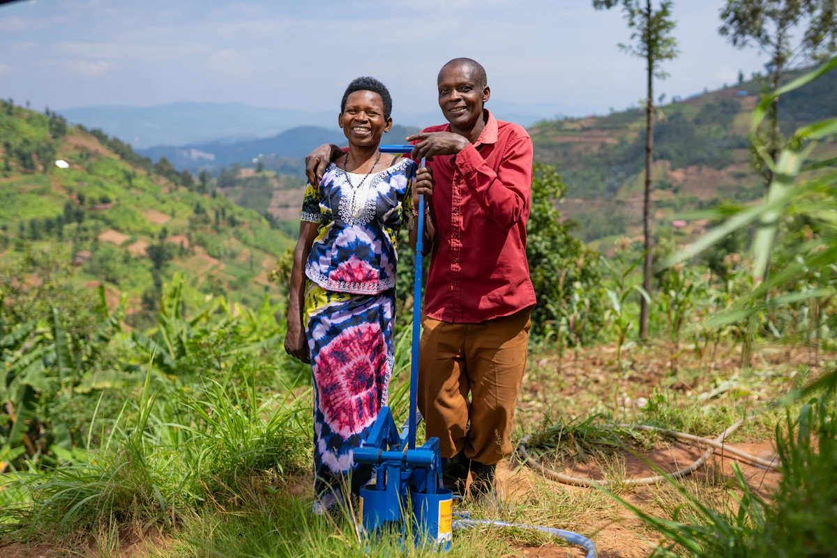 Two farmers stand beside an irrigation pump in a hillside field in Rwanda.