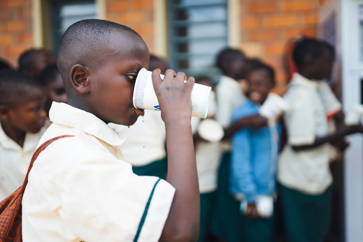 A student drinks clean water from a cup at a school in Rwanda while other students wait nearby.