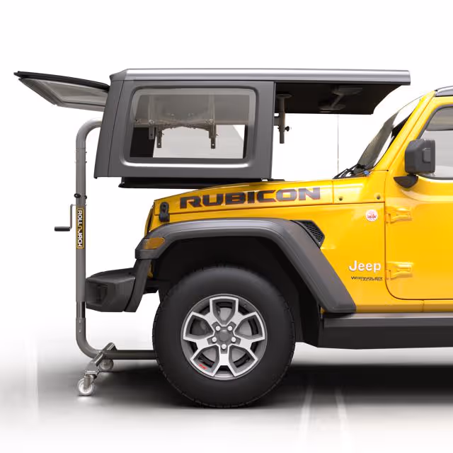 Yellow Jeep Rubicon with a gray rooftop storage box mounted on the rear and supported by a metal frame with wheels.