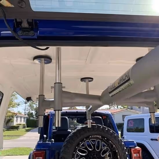 Interior view of a vehicle with a mounted gun rack holding multiple rifles, visible through the back window with a spare tire attached outside.