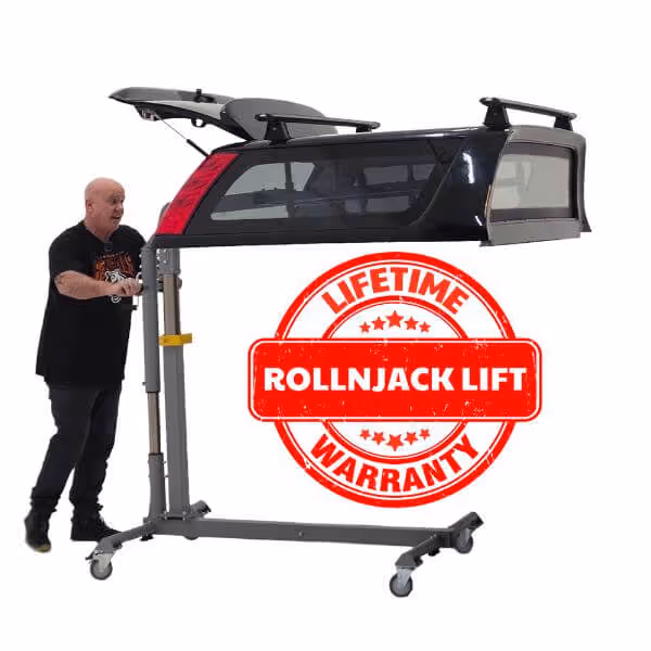 Man operating a RollNJack Lift to raise a black truck camper shell, with a red stamp displaying 'Lifetime Warranty'.
