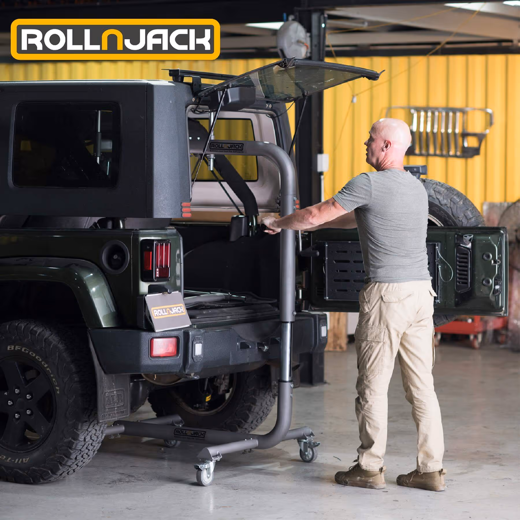 Man operating a RollnJack vehicle lift next to a dark green SUV with its rear door open in a garage.