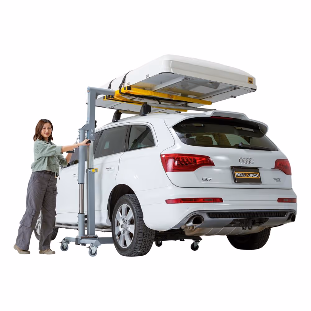 Woman operating a portable car lift to raise a roof cargo box on a white Audi Q7 SUV.