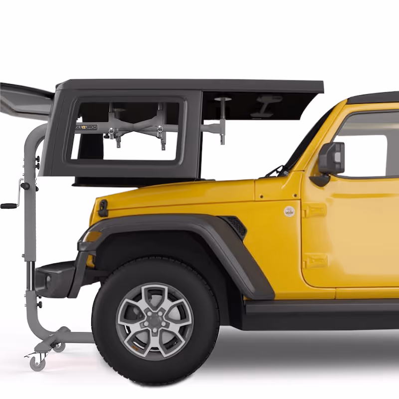 Yellow Jeep with a black detachable hardtop being lifted off or placed on by a mechanical hoist.