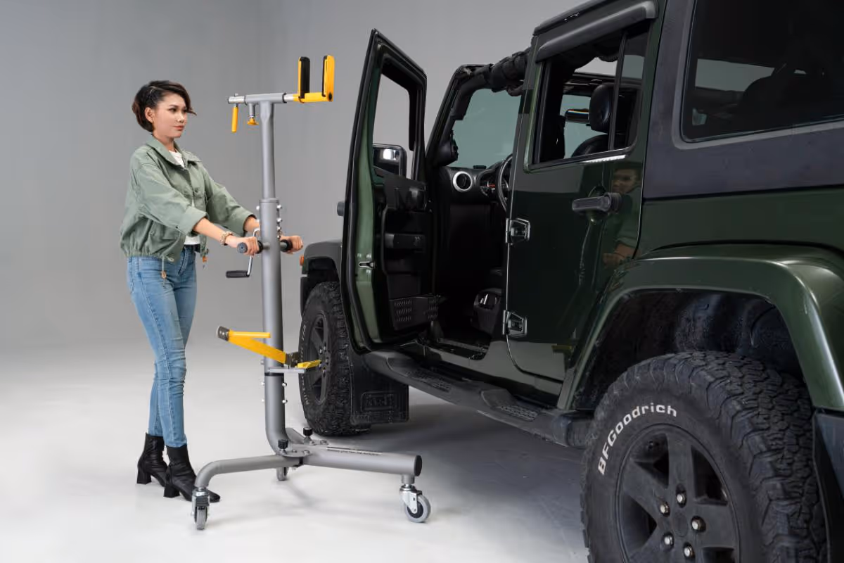 Woman adjusting a bike repair stand beside a green Jeep with open driver door in a studio setting.