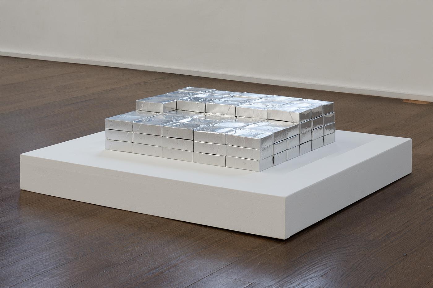 Naoki Sutter-Shudo, Work, Early 21st century, ongoing. Flame retardant aluminum foil tape on emptied cigarette packs. Variable dimensions. Each module is 3.5 x 1 x 2.2 in (8.9 x 2.5 x 5.6 cm). Fee: 220 minutes of life reserve depleted to be compensated at the current minimum wage of the artist's state of residence, per module