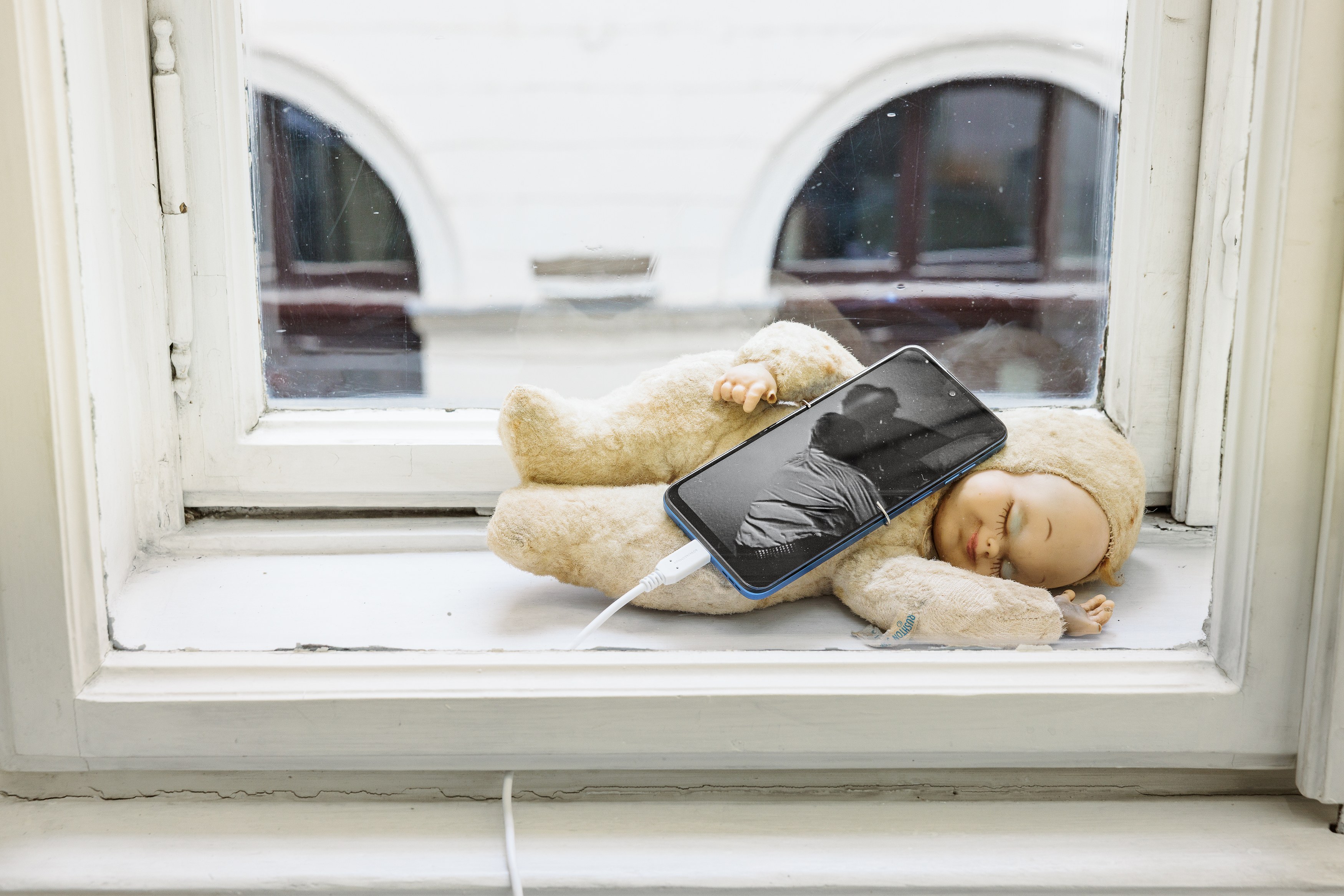 Nicole-Antonia Spagnola, Old Baby (Reverse Kiss), 2026, Doll, smartphone, USB-C charger, 8mm to Mp4 (B/W), 32 × 18 × 12 cm (12 5/8 × 7 1/8 × 4 3/4 in). Courtesy of the artist and Felix Gaudlitz.