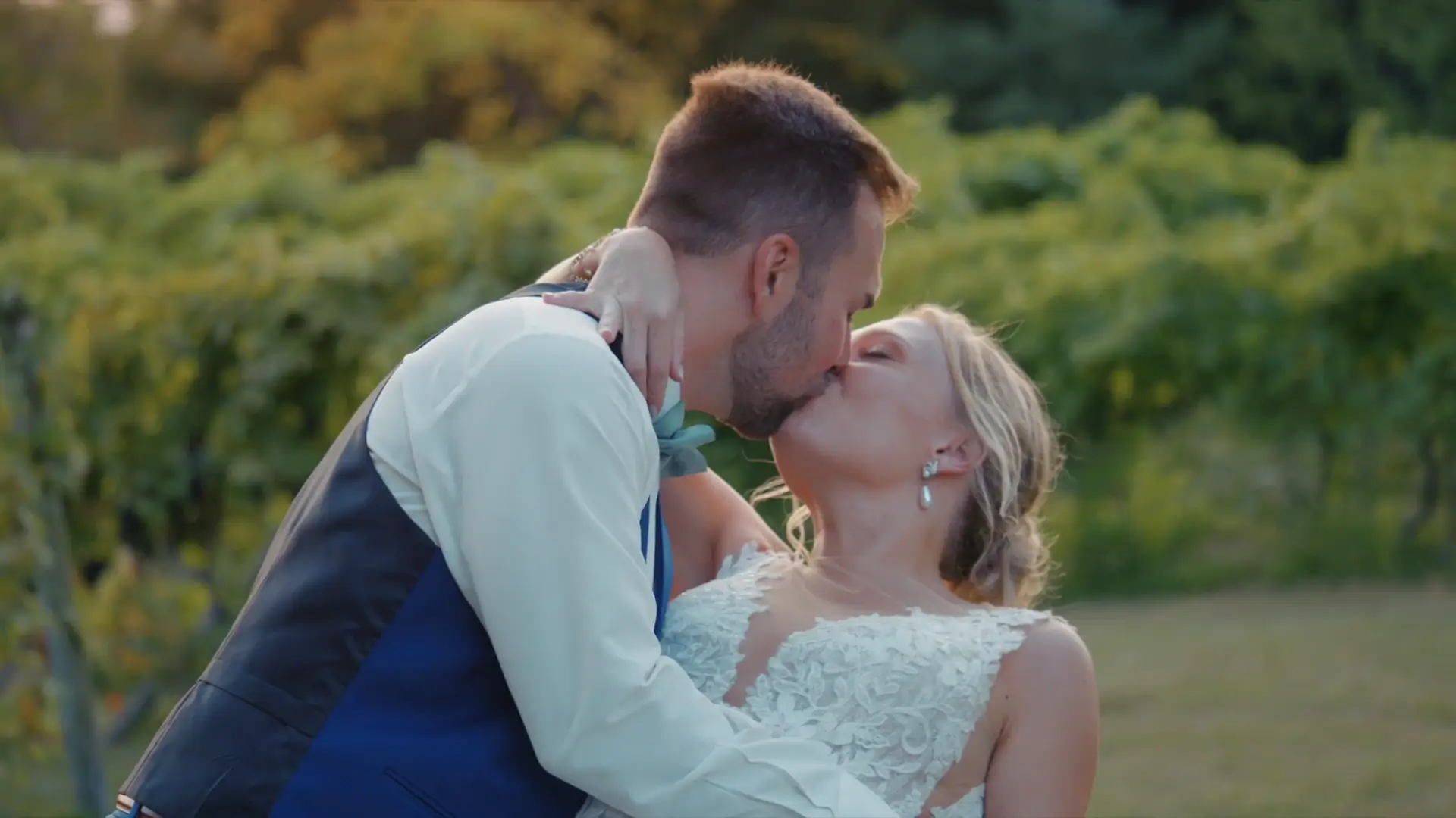 Lindsey and Joey share a kiss in this romantic snapshot from their wedding video. The vineyard greenery of Ciccone Vineyard and Winery enhances the background, capturing the essence of their special day in Suttons Bay, Michigan.