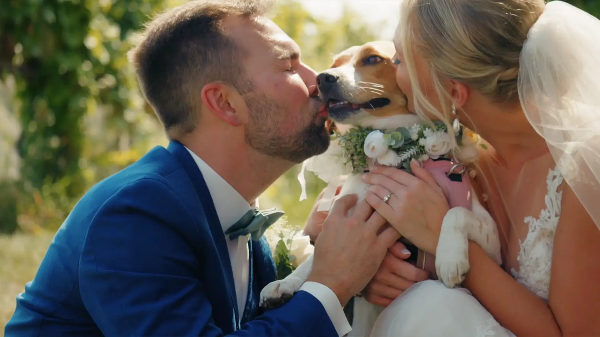In this tender moment captured by their wedding videographer, Lindsey and Joey share a kiss with their dog, who is adorned with a floral collar at Ciccone Vineyard and Winery.