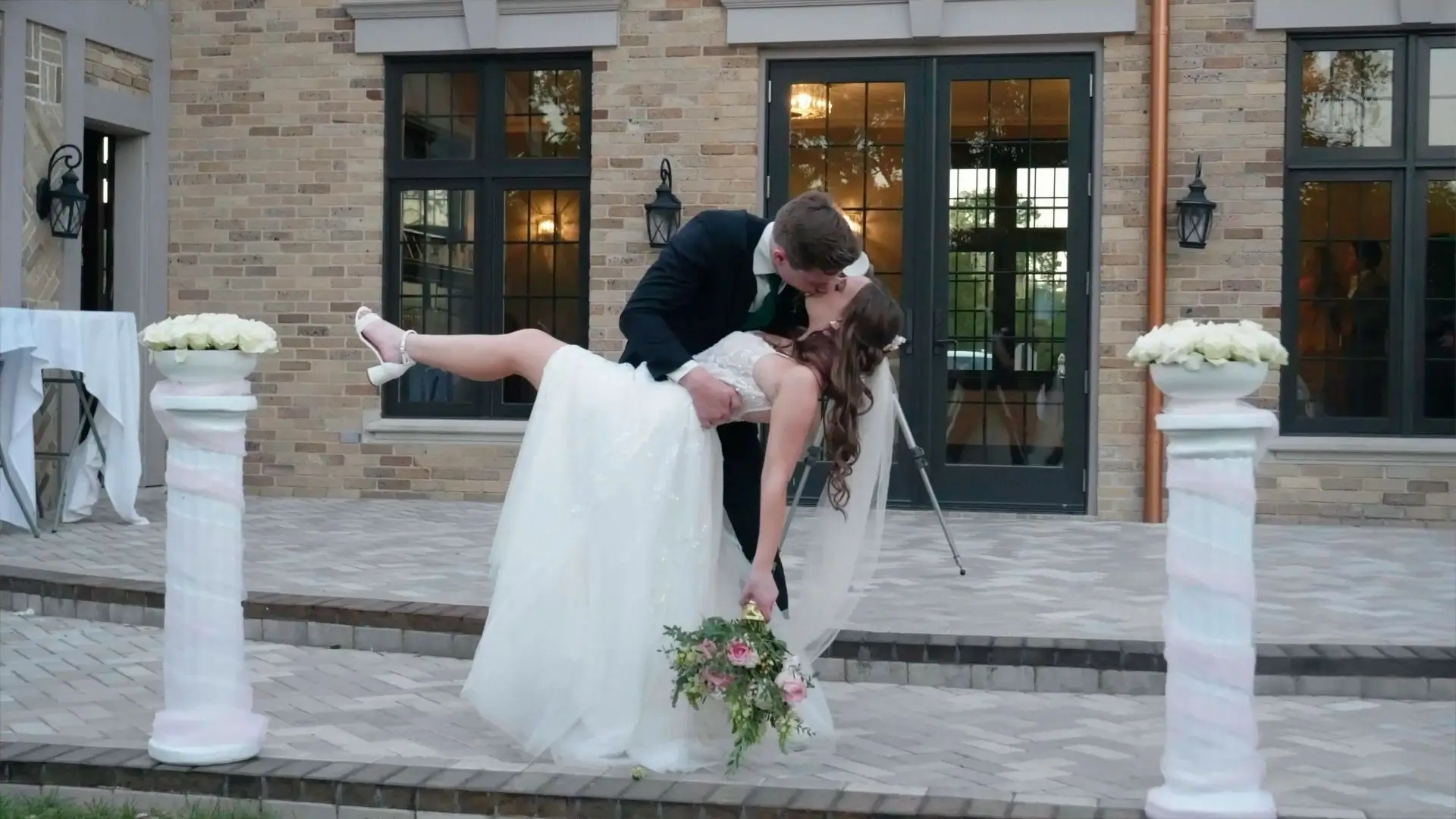 In this romantic snapshot from Maddie and Jack's wedding video, the groom dips and kisses the bride in front of the elegant Venue3Two backdrop in Grand Rapids, Michigan, capturing a joyful moment in their celebration.
