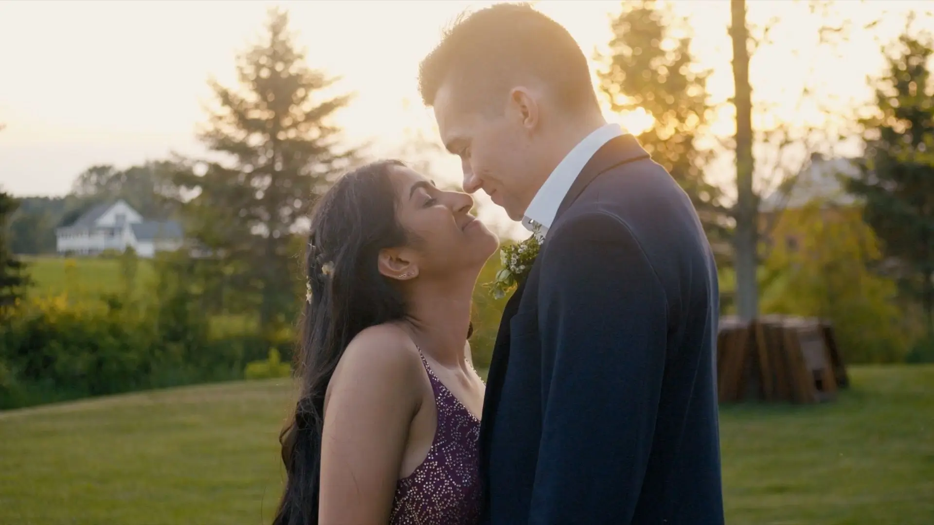 Anushka and Sean share a heartfelt moment, nose-to-nose, against a backdrop of lush Michigan greenery at The Valley at Frutig Farms in Ann Arbor. Anushka wears a vibrant dress, while Sean is in a dark suit, with the sun setting behind them.