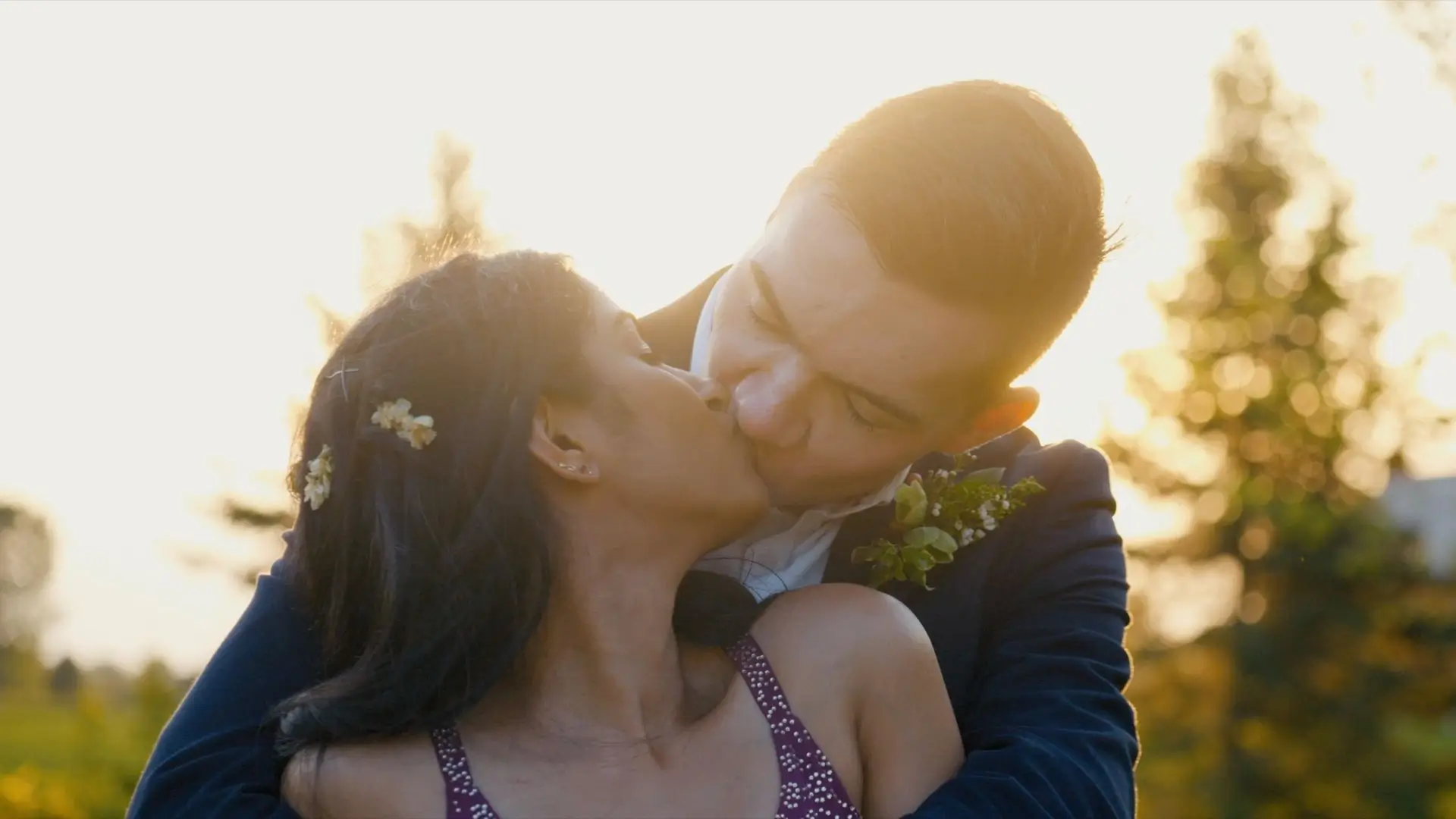 Anushka and Sean share a kiss at sunset in a tender moment captured by their wedding videographer. They are surrounded by picturesque Michigan greenery, with the golden light creating a romantic backdrop. Anushka's hair is adorned with small flowers.