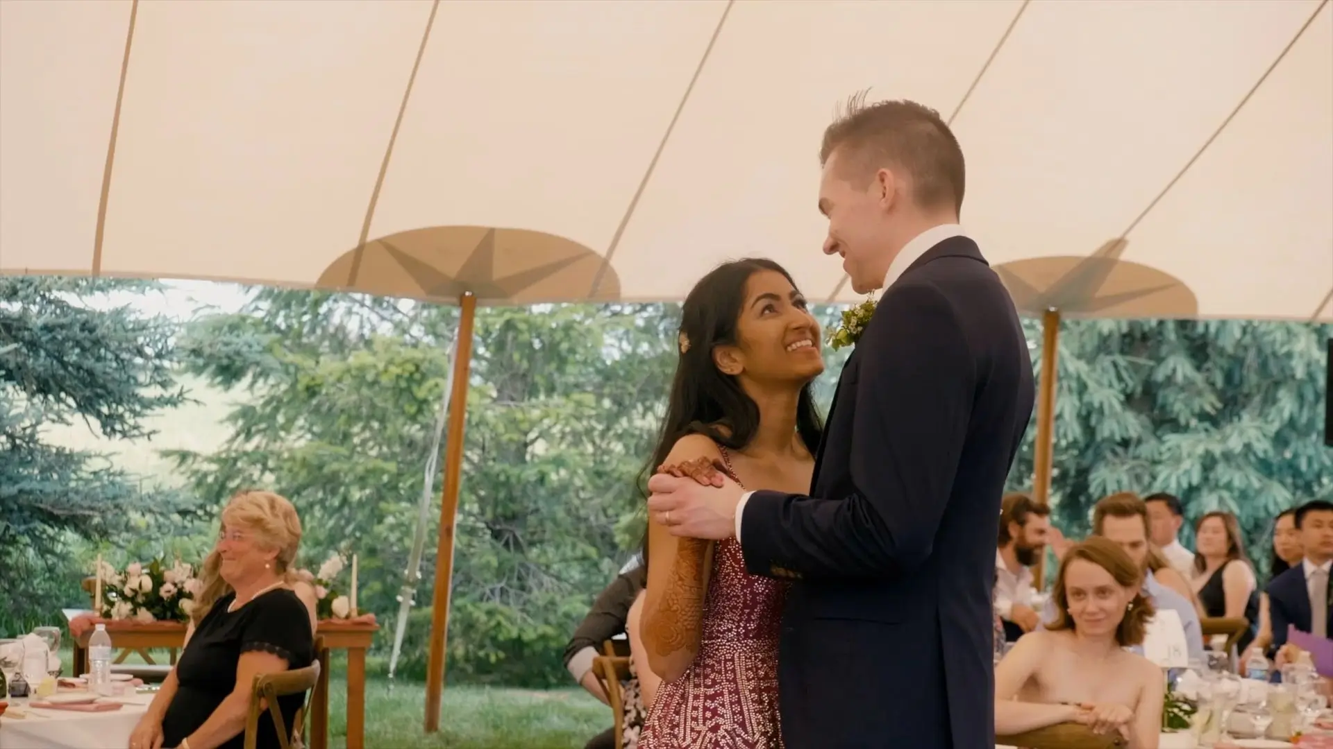 Anushka and Sean share a tender moment dancing under a tent at The Valley at Frutig Farms, surrounded by lush Michigan greenery. This heartfelt snapshot from their wedding videographer captures the joy and love in the air as guests look on with smiles.