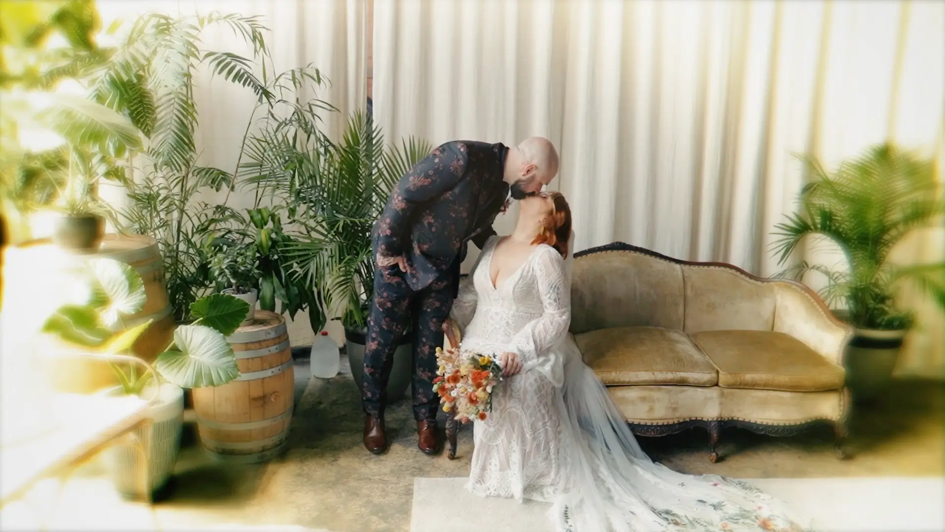In this whimsical snapshot from their Michigan wedding video, the bride and groom share a loving kiss amidst lush greenery, embodying their hipster aesthetic. The scene highlights their natural, loving vibe captured by the wedding videographer.