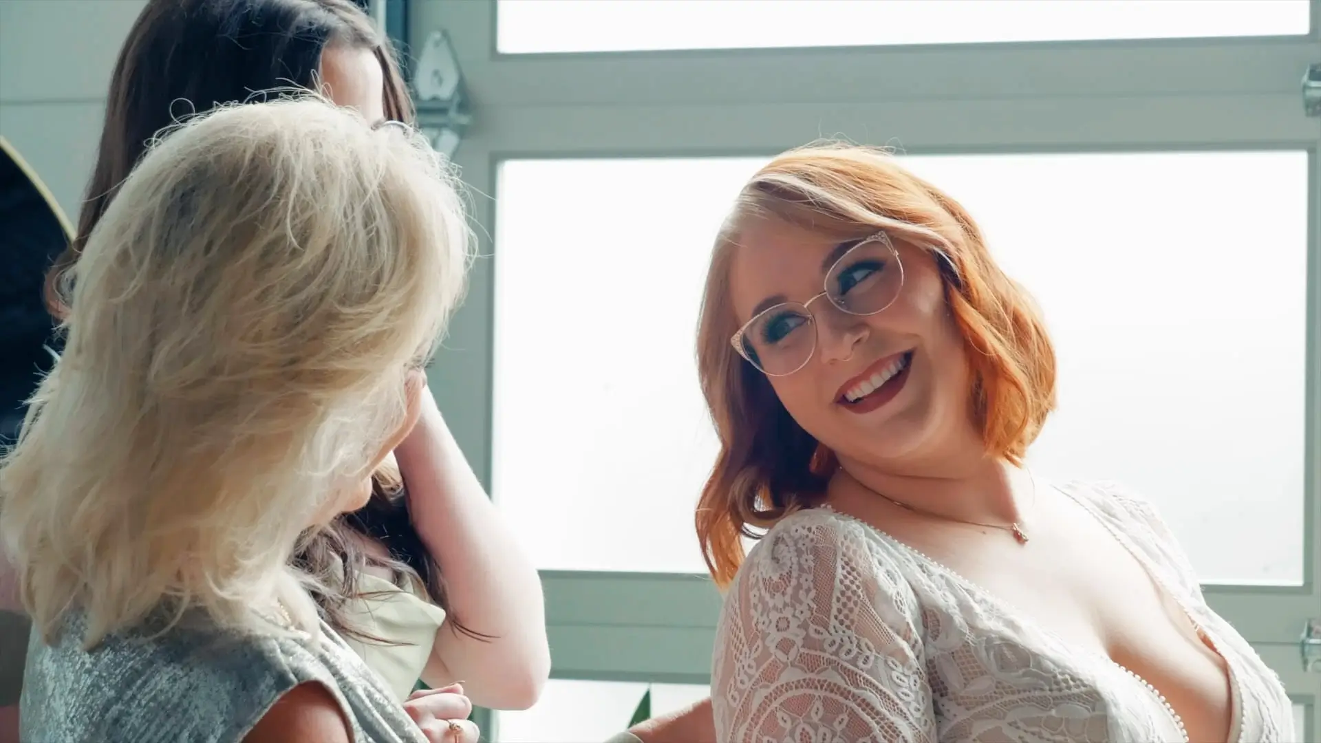 In this wedding videography moment, a joyful bride in a lace dress smiles warmly at a friend inside the Michigan venue. The soft lighting adds to the intimate ambiance of their special day.