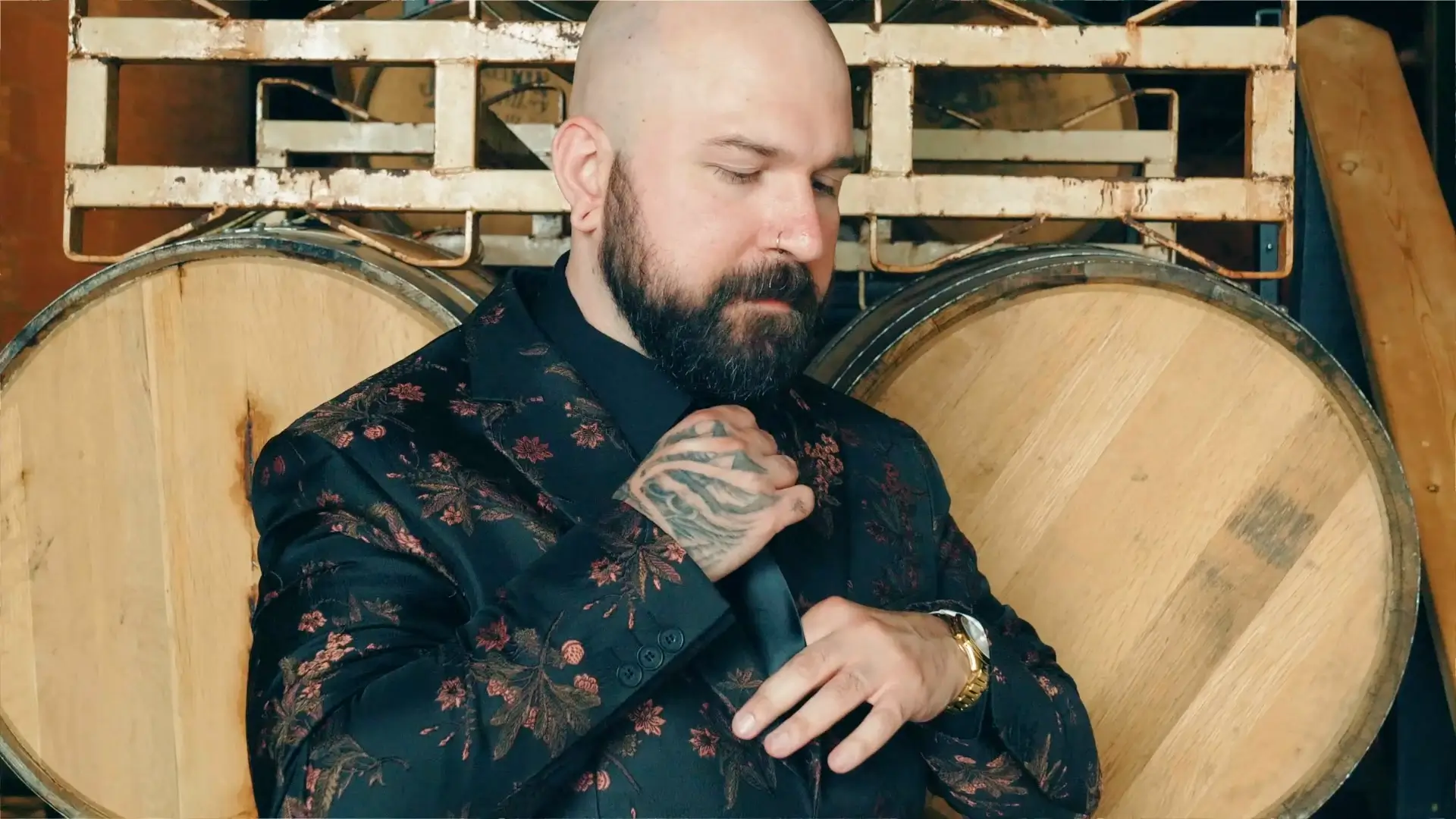 A man in a floral suit adjusts his tie in front of wooden barrels, symbolizing the rustic charm of Michigan.