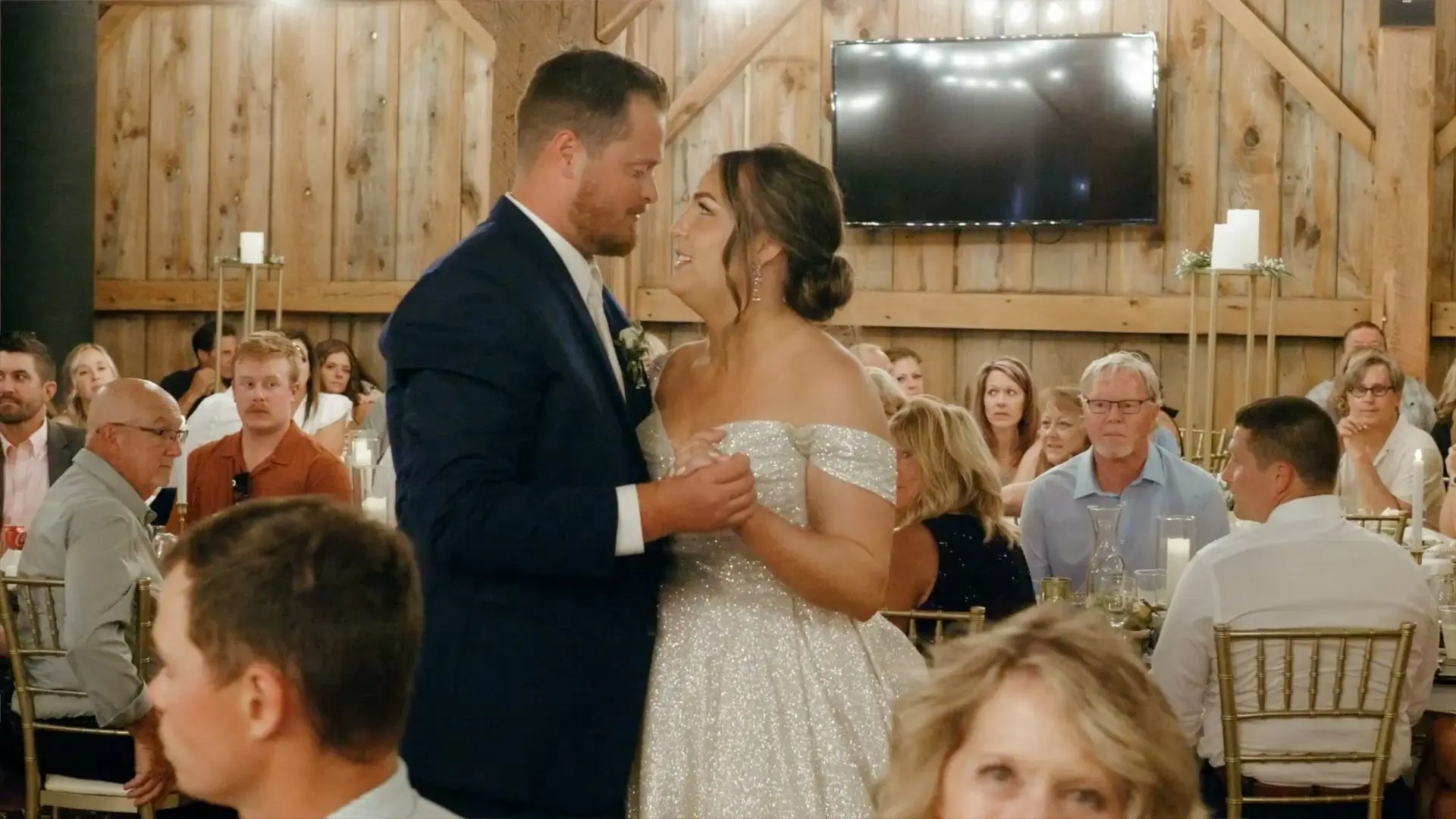 In this still from their wedding at Sonshine Barn in Gaylord, Brittany and Dakota share a joyful first dance, surrounded by seated guests who watch and smile. The barn's rustic wooden interior creates a cozy backdrop for the celebration.
