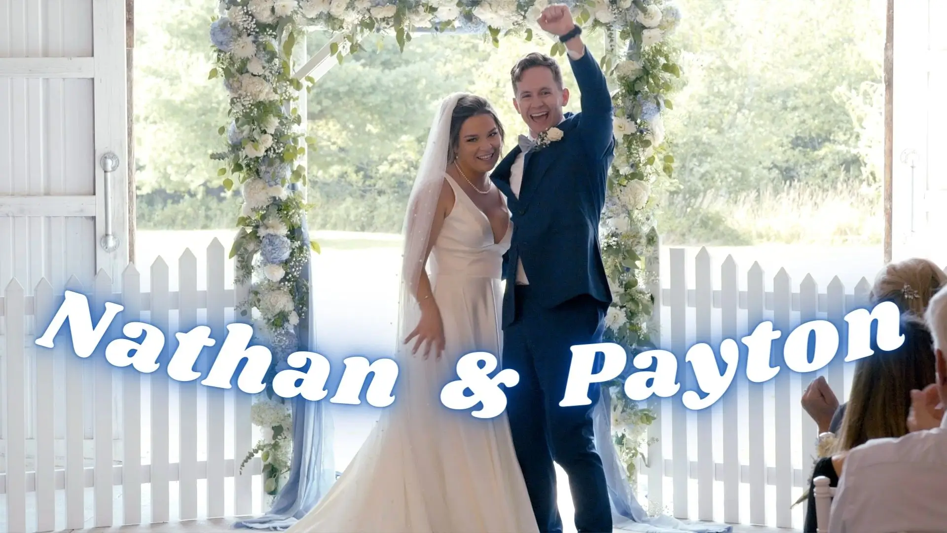 Nathan and Payton smile and celebrate at their wedding under a floral arch at Treetop Meadows, Ludington, Michigan. This joyful moment is captured in a still from their wedding video, with the vibrant Michigan greenery in the background.