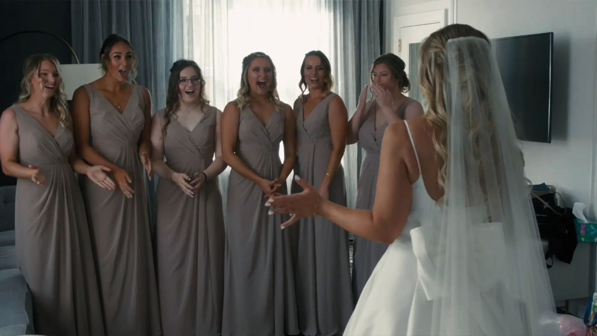 Bridesmaids react joyfully as the bride reveals her dress in this touching moment captured by the wedding videographer at Amway Grand Plaza, Grand Rapids.