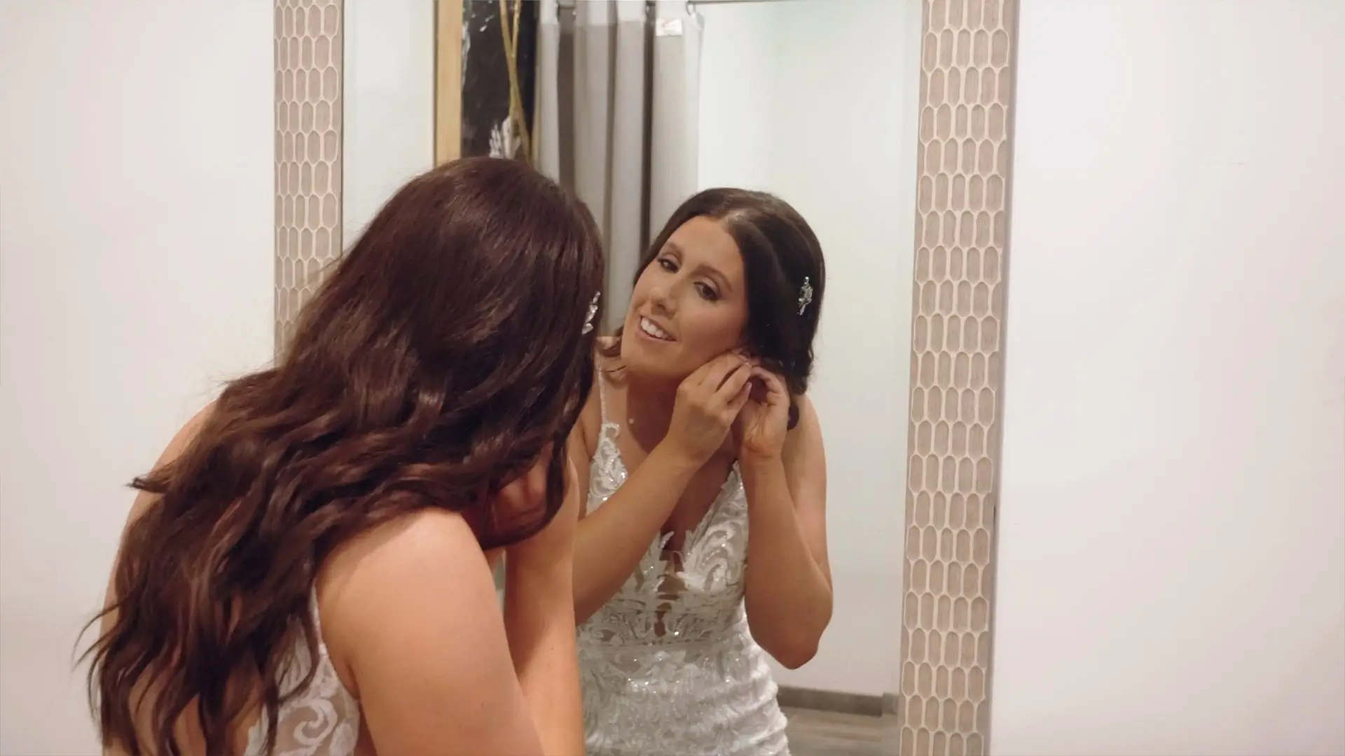 Amanda, in her wedding dress, adjusts her earrings while looking in a mirror at Rooster Ridge Vineyard in New Era.