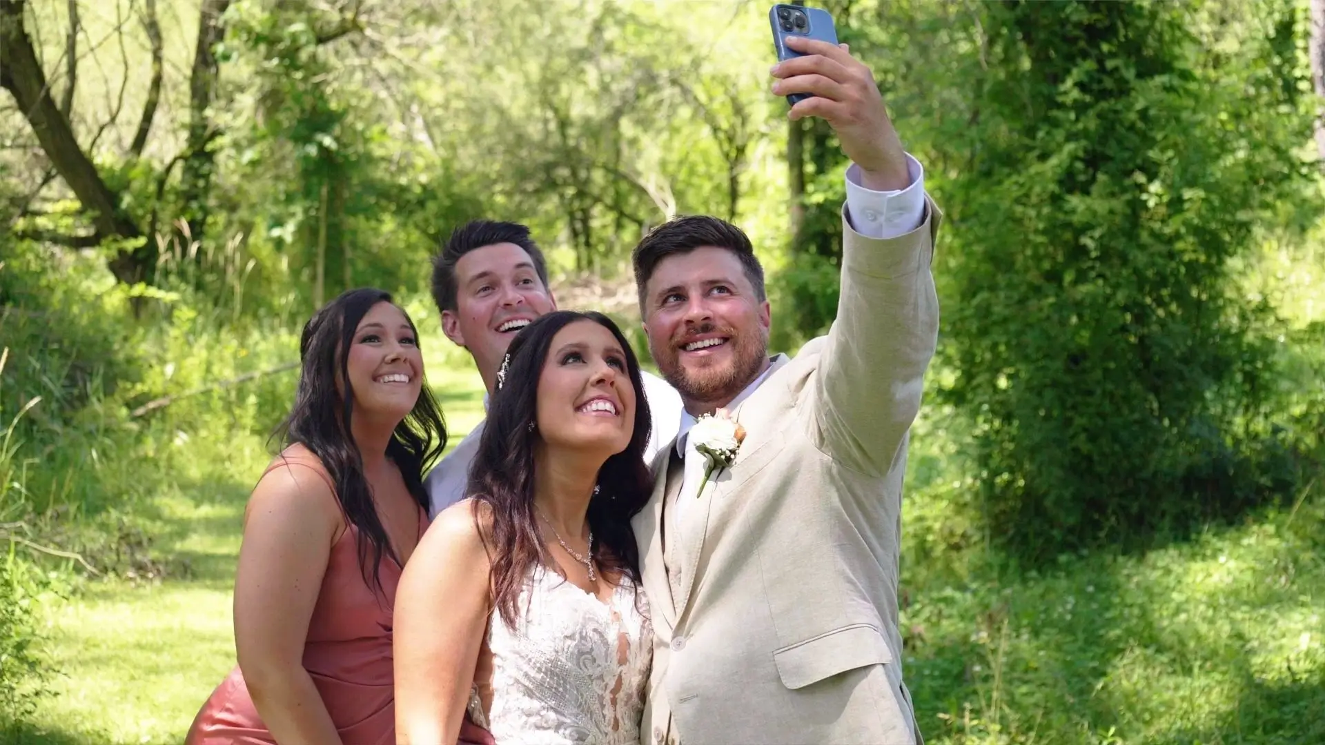 The bride and groom, Amanda and Isaac, pose for a selfie with their wedding party in the lush greenery of Rooster Ridge Vineyard. This snapshot captures their joy and the vibrant surroundings, commemorated by their wedding videographer.