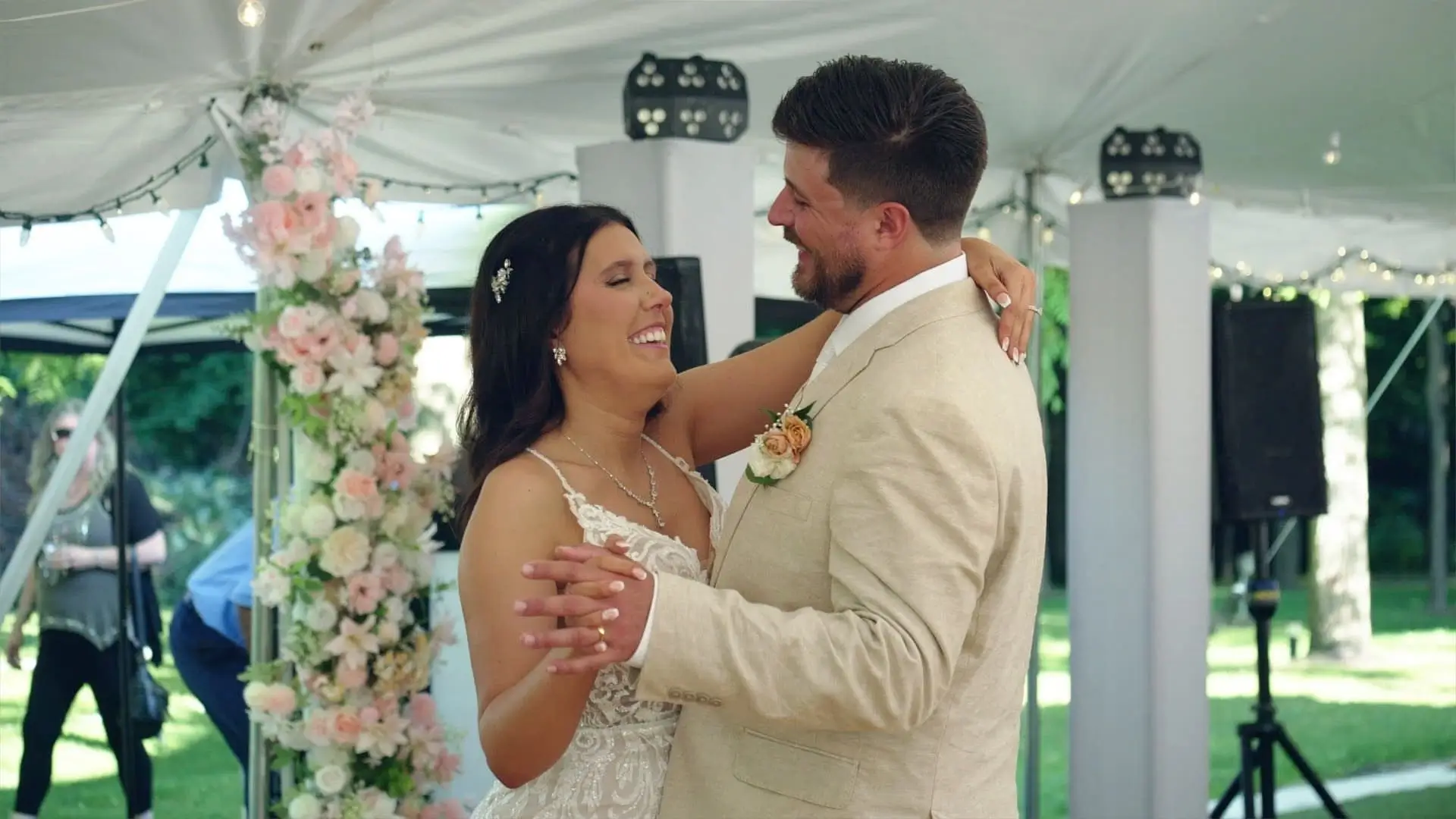 n this still from their wedding video, Amanda and Isaac share a joyful dance at their reception at Rooster Ridge Vineyard in Michigan. Surrounded by floral arrangements and greenery, the scene captures the cozy and loving atmosphere of their special day.