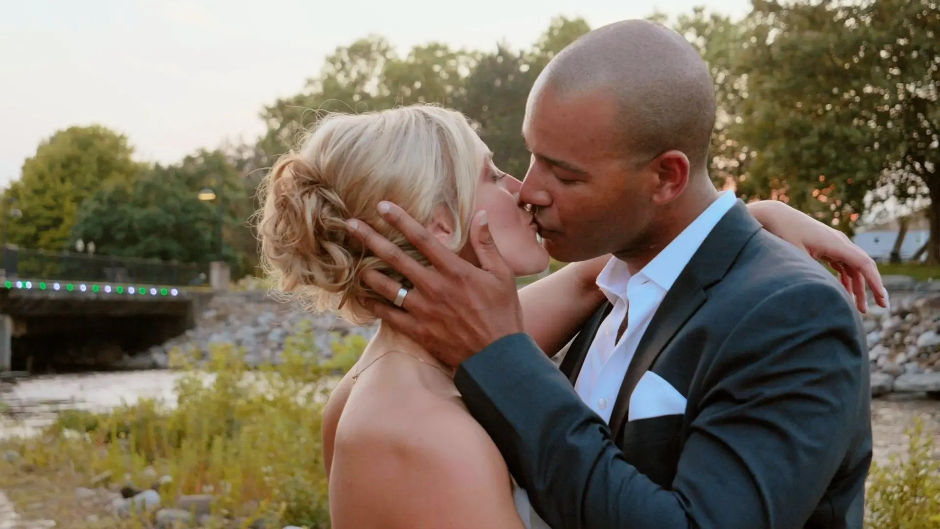 Bride Kasey and groom Roberto share a romantic kiss against a backdrop of lush Michigan greenery and a serene riverside in Battle Creek, Michigan.