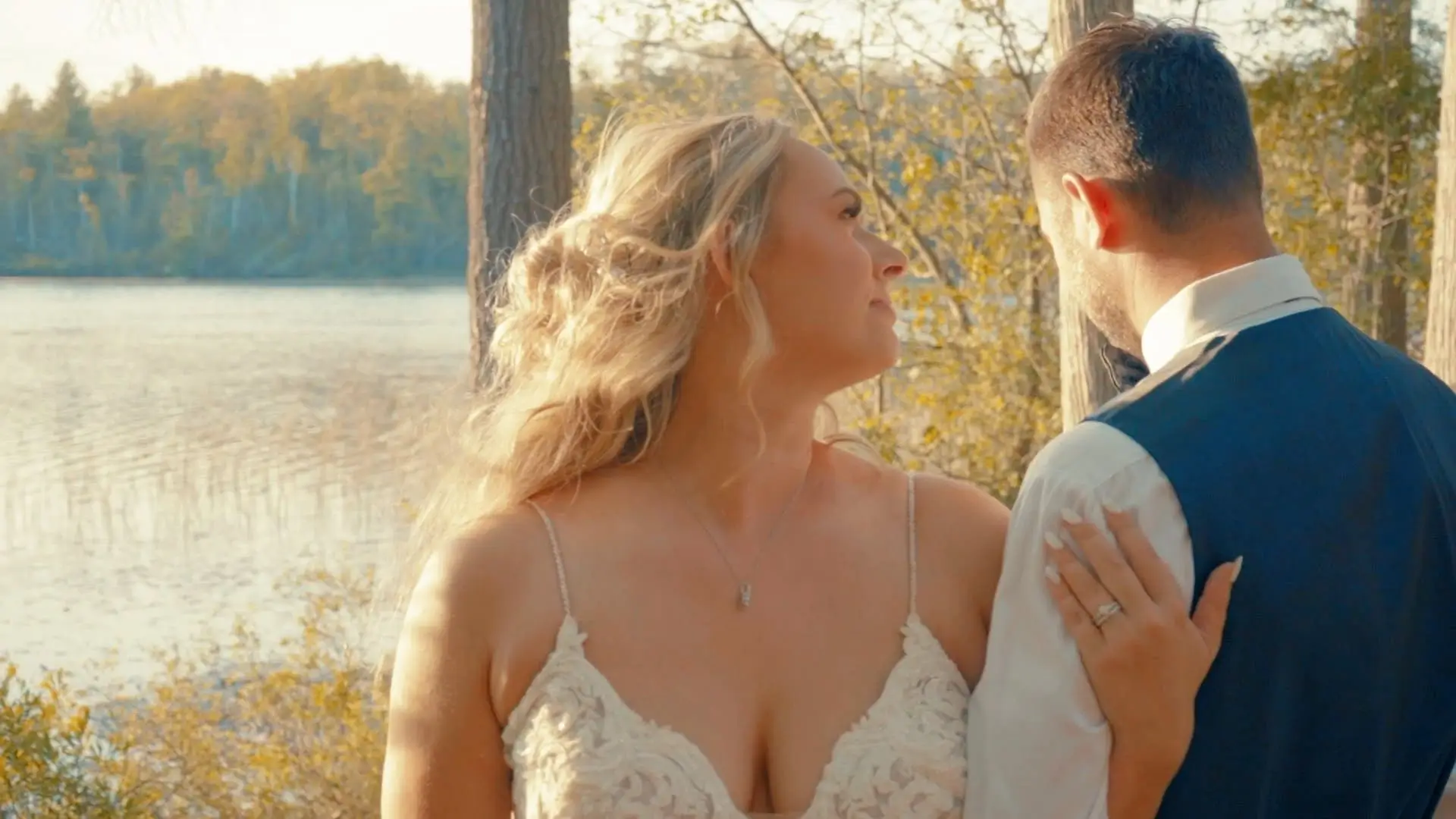 Newlyweds Caroline and Matt share a tender moment by a serene Michigan waterfront, with Caroline's hand resting on Matt's shoulder, capturing the joy of their wedding day.