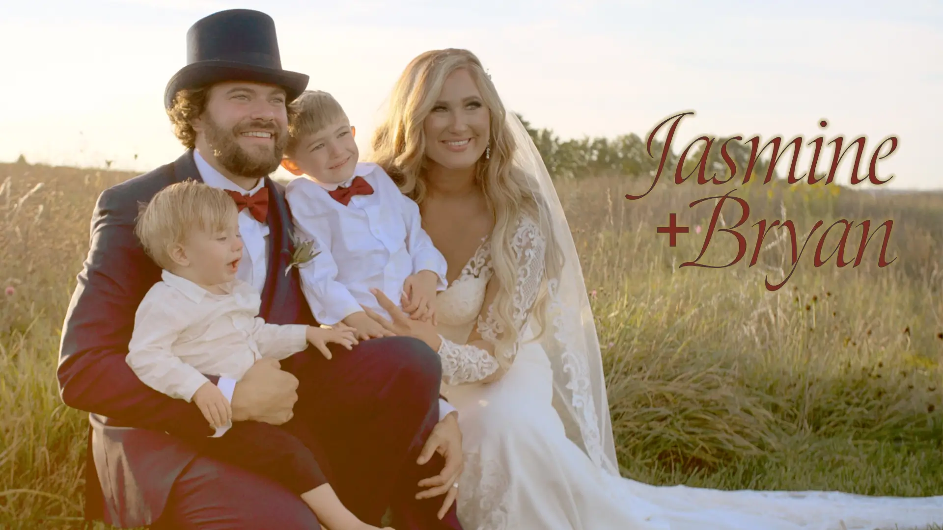 A newly married couple, Jasmine and Bryan, sit smiling in a field with their two sons, Remington and Briggs. Bryan, in a top hat and suit, holds the younger son, while Jasmine, in a lace wedding dress, holds the older son. Text reads "Jasmine + Bryan."