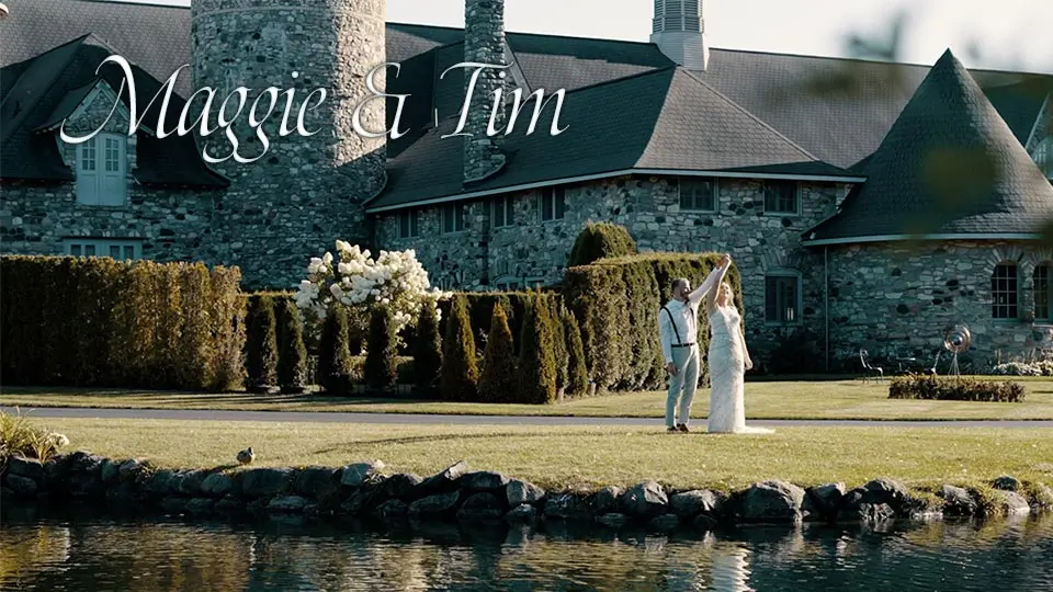 Maggie and Tim are dancing on the lawn in front of Castle Farms, a picturesque stone venue in Michigan. The names "Maggie & Tim" are displayed above them. The scene includes well-manicured gardens and a calm pond in the foreground.