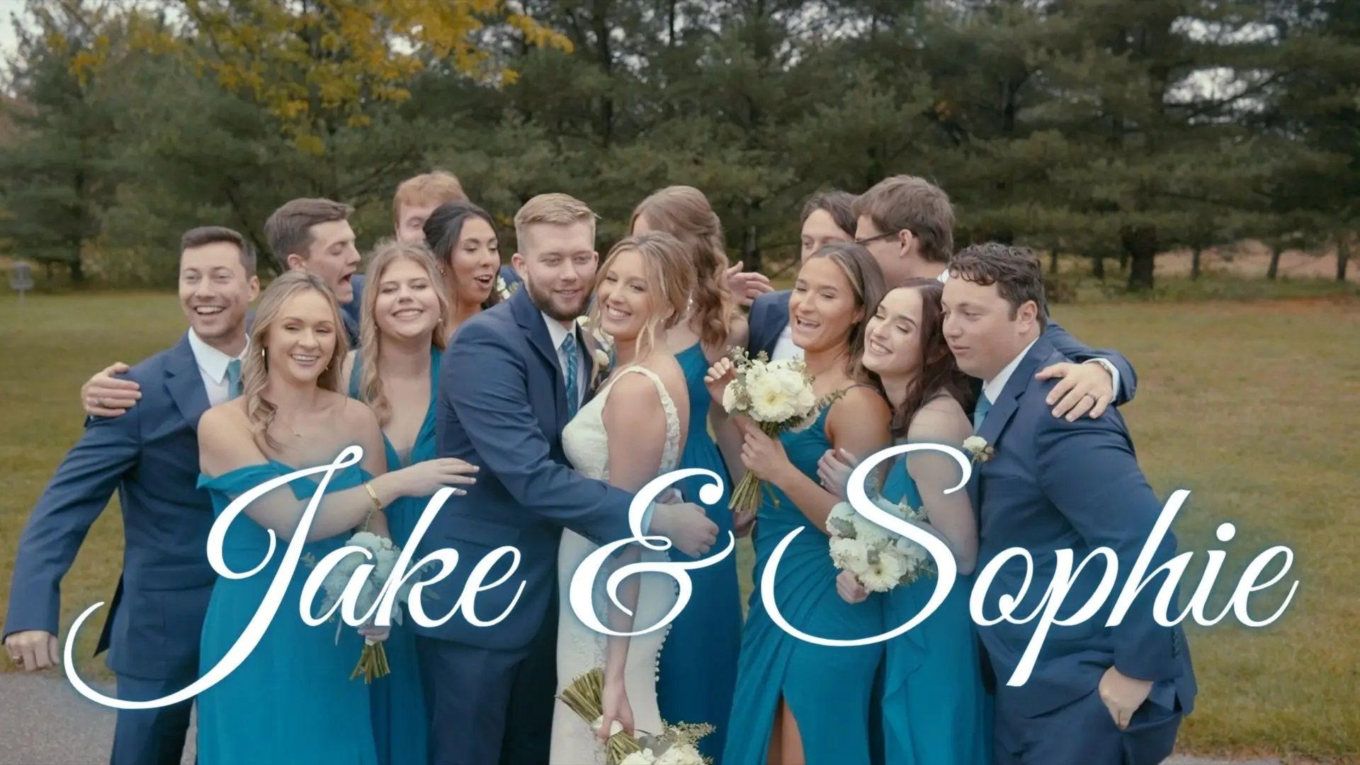 A wedding party of 12 smiles outdoors, focusing on the bride and groom, Sophie and Jake. The bridesmaids wear blue dresses and the groomsmen wear blue suits. "Jake & Sophie" is overlaid in white cursive script against a backdrop of trees and grass.