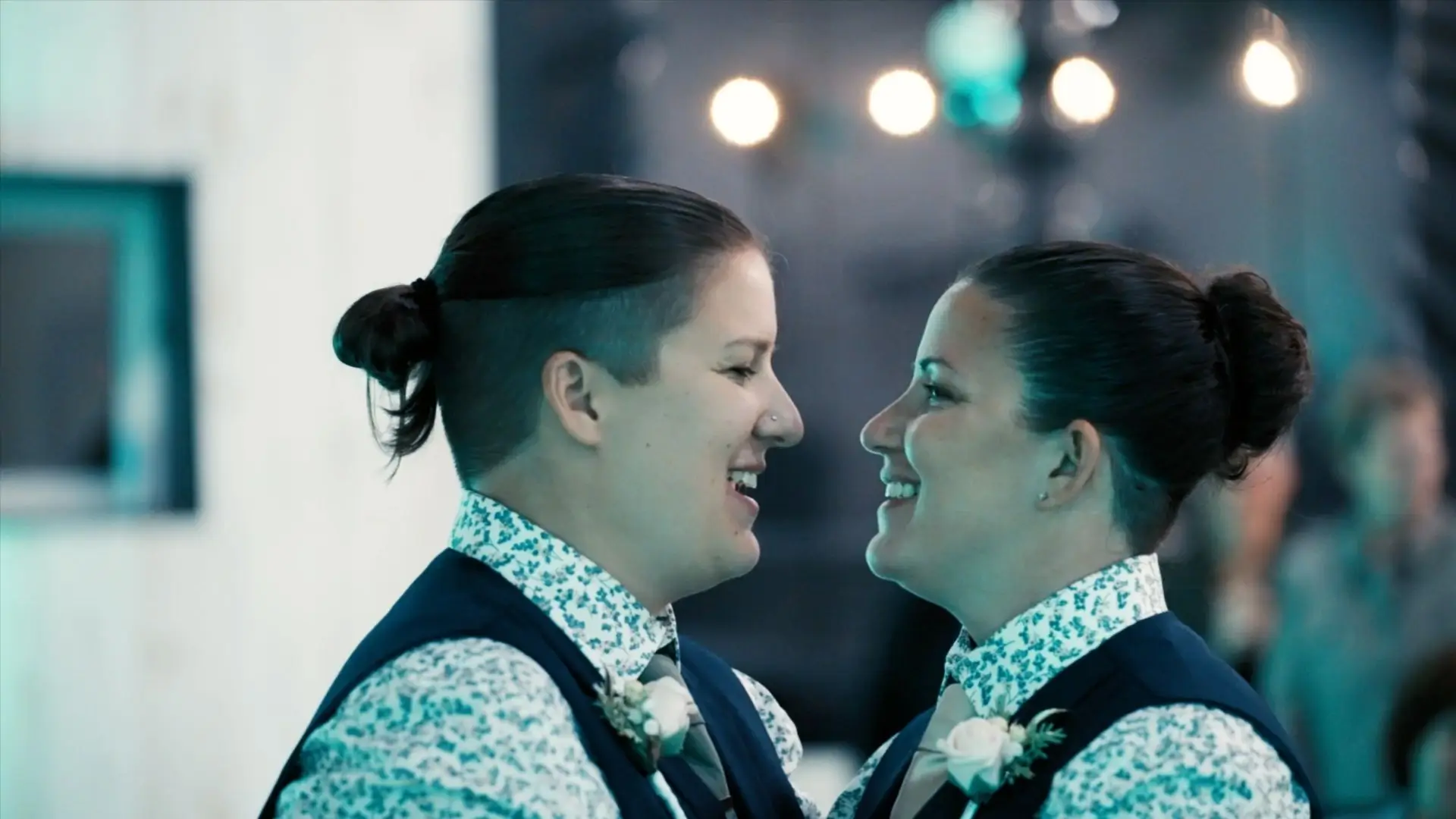 Alexis and Carly share a joyful moment during their wedding dance, dressed in coordinated vests and floral shirts. Captured by their videographer at Jacob's Farm in Traverse City, the couple beams with happiness and love.